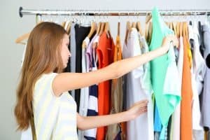 Beautiful young woman  thinking what to dress near rack with hangers