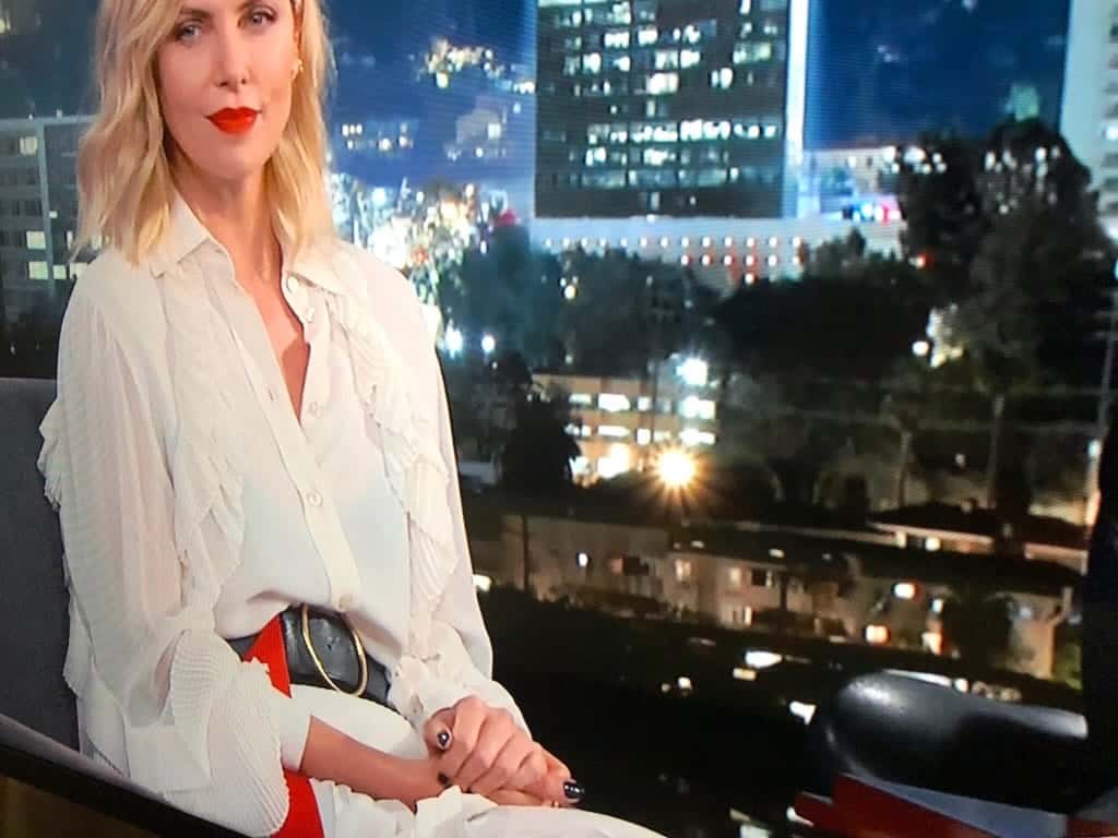 Charlize Theron wearing a long belt over a white dress on Jimmy Kimmel Live.