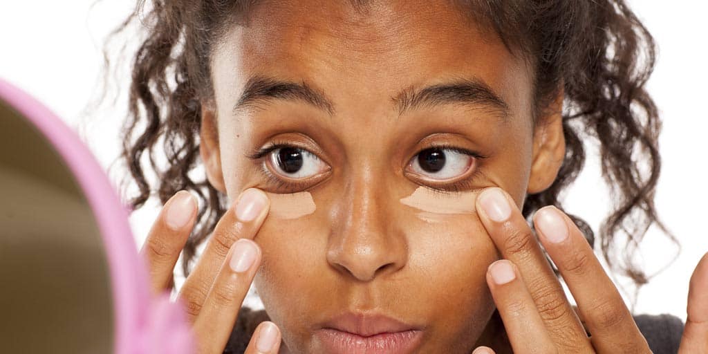 Woman putting on concealer over puffy eyes.